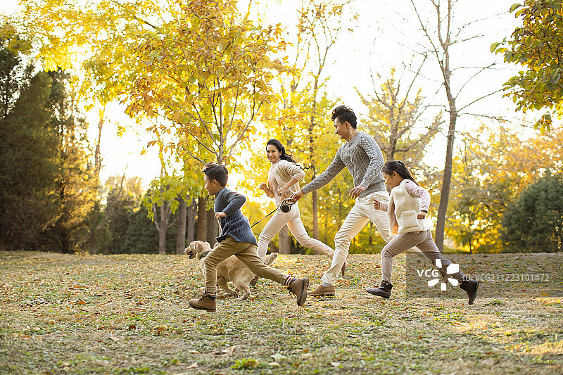 快乐的年轻家庭和狗在秋日的树林里图片素材