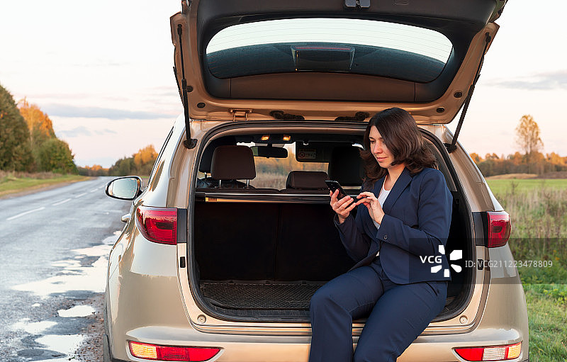 在汽车后备箱上玩手机的女孩图片素材
