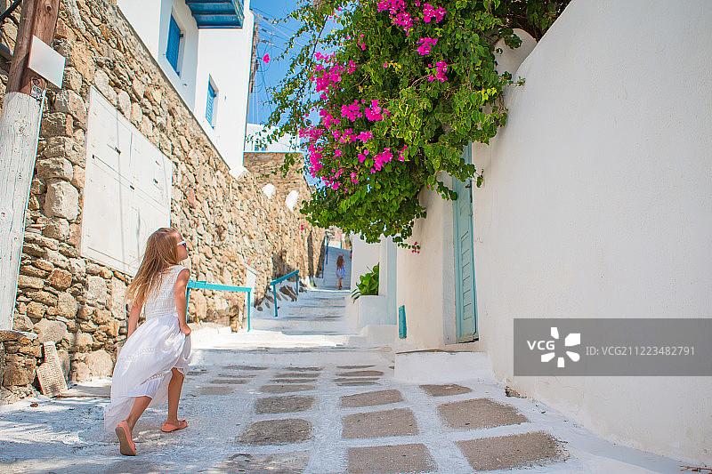 在典型的希腊街道上玩耍的可爱白裙小女孩图片素材