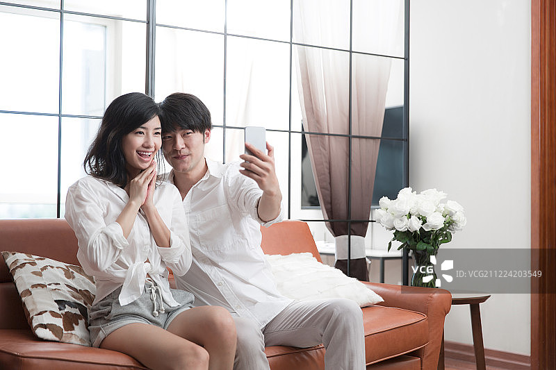 青年情侣在客厅拿着手机自拍图片素材