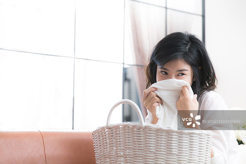 年轻女子在客厅拿着衣服闻感受清新图片素材