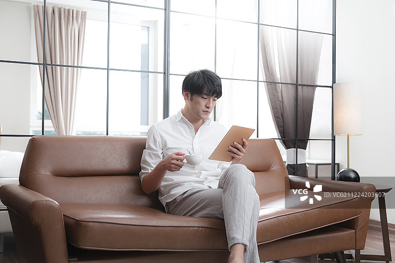 青年男子在客厅喝咖啡使用平板电脑图片素材