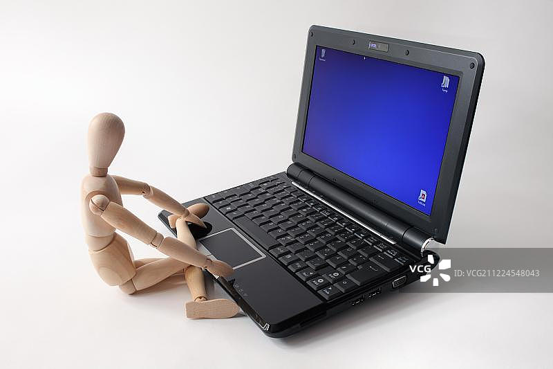 坐在笔记本电脑前的木制玩偶图片素材