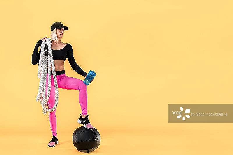 穿着粉色和黑色运动服，手持粗绳和摇壶的迷人女子，背景为黄色图片素材