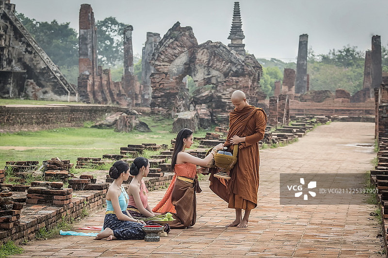 身穿泰国传统服饰的年轻女子向僧侣致敬图片素材