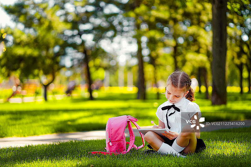 放学后坐在草地上，背着粉色背包的女孩图片素材