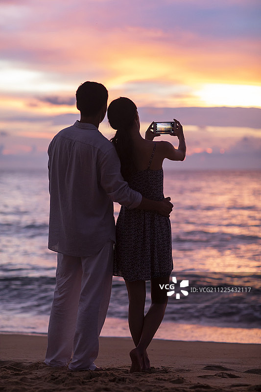 年轻情侣在海边使用手机拍摄海景图片素材