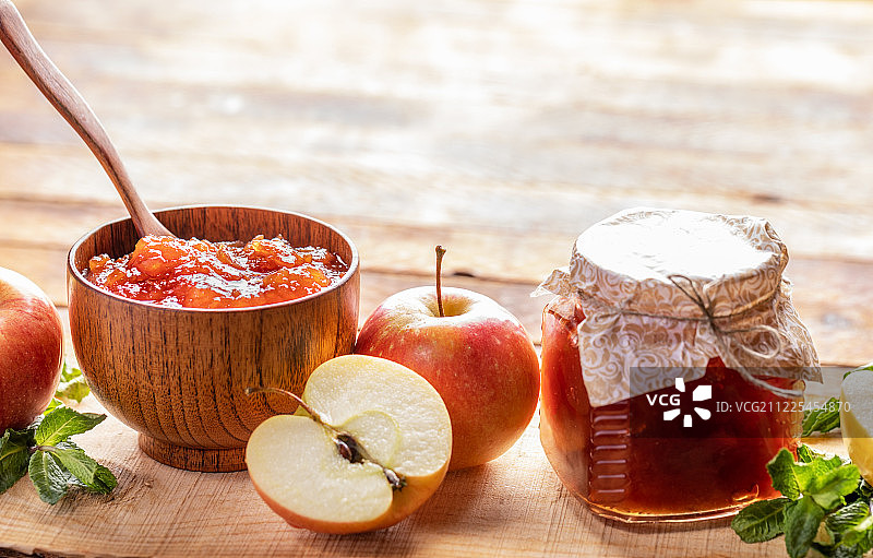 特写：木碗和玻璃罐，内有苹果酱、苹果和绿色薄荷，木质背景图片素材