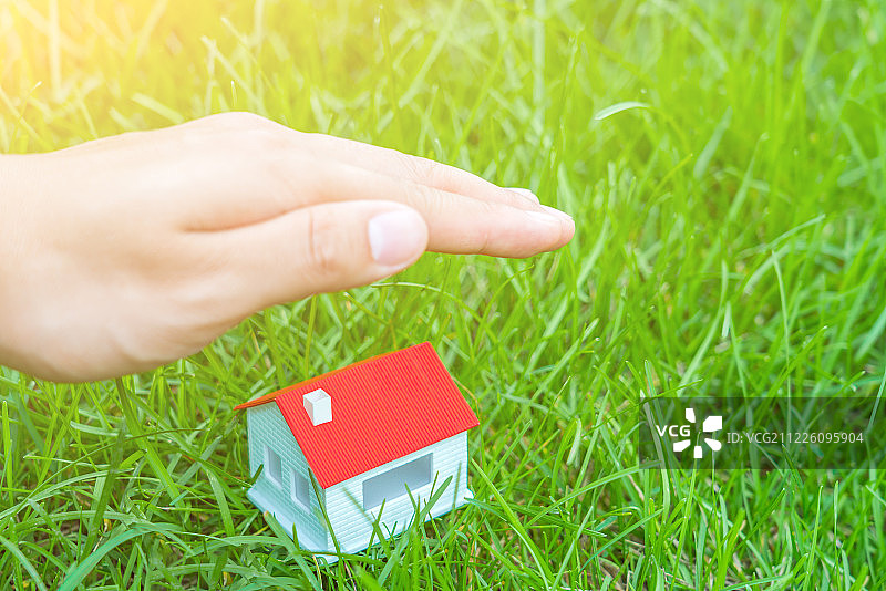 一双手呵护着草地上的小房子——保险业感念图片图片素材