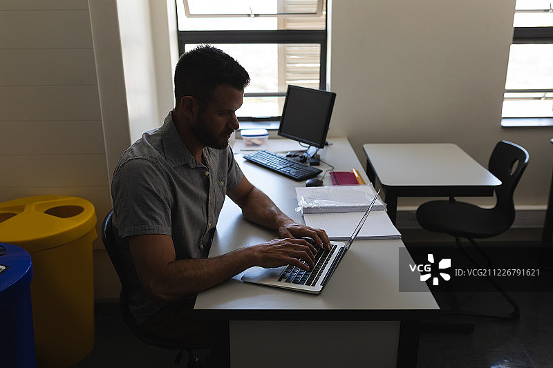 在教室书桌旁使用笔记本电脑工作的学校老师侧面照图片素材