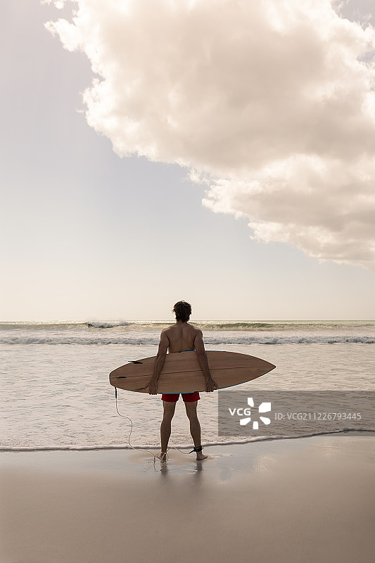 站在海滩上拿着冲浪板的年轻男人图片素材