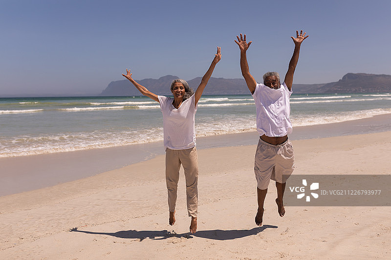 在海滩上举起双臂跳跃的老年夫妇图片素材