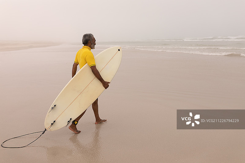 年长的男人带着冲浪板在海滩上行走图片素材