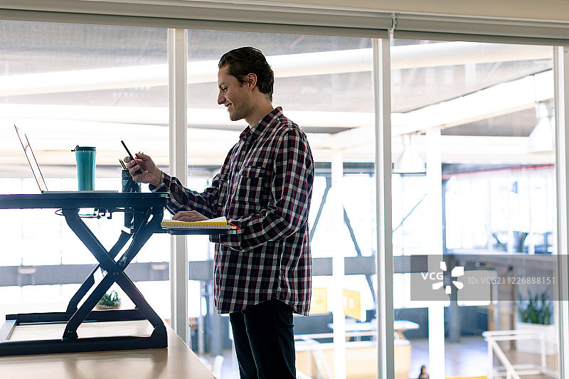 在办公桌前用笔记本电脑和手机的男平面设计师图片素材