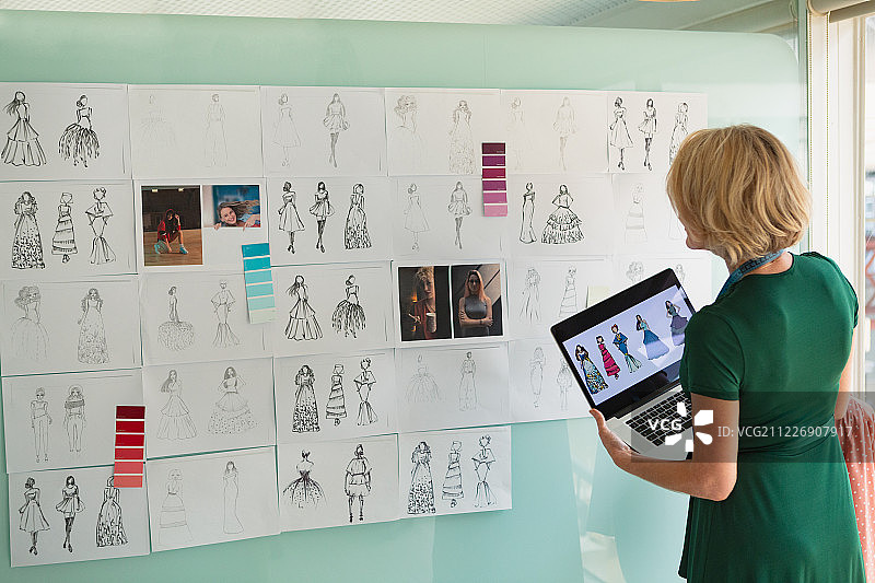 女时装设计师在设计工作室里看着草图，同时拿着笔记本电脑图片素材