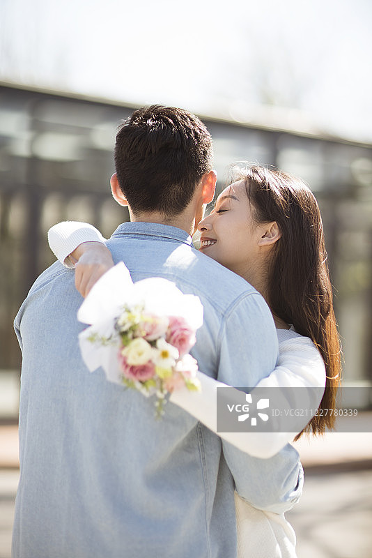 年轻女子手拿鲜花拥抱男朋友图片素材
