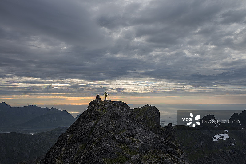 挪威罗弗敦群岛弗拉克斯塔社区最高峰，斯特恩廷德山顶上日落时分的女徒步旅行者远景图片素材