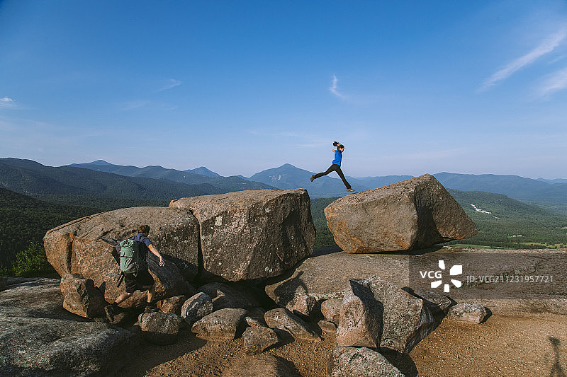 在纽约州阿迪朗达克山脉Pitchoff山，有冒险精神的女徒步旅行者跳过巨石图片素材