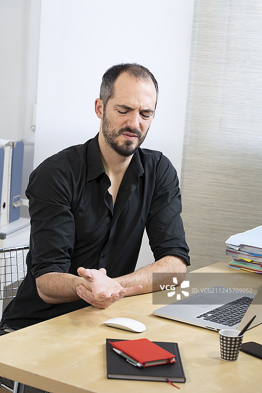 手腕疼痛坐在办公桌前的男人图片素材