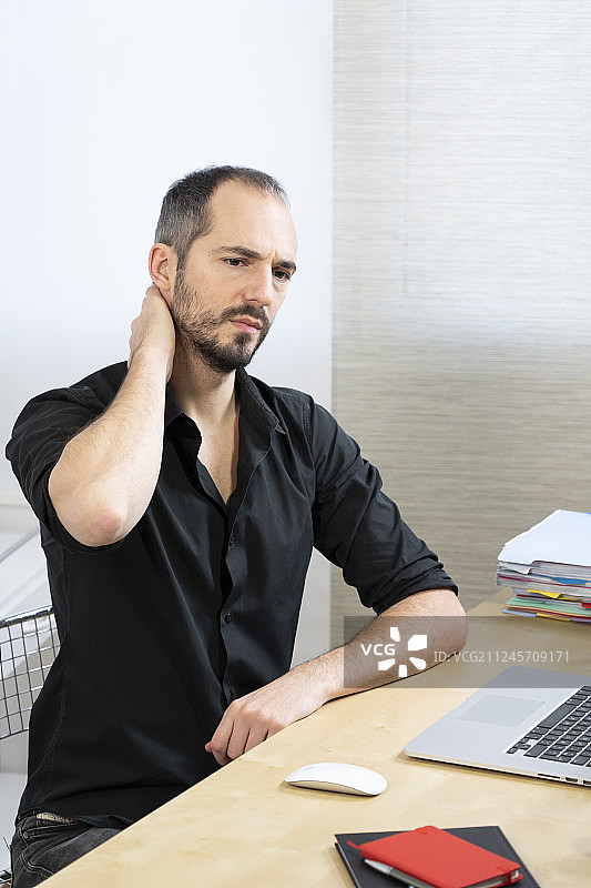 男子在办公桌前感到颈部疼痛图片素材