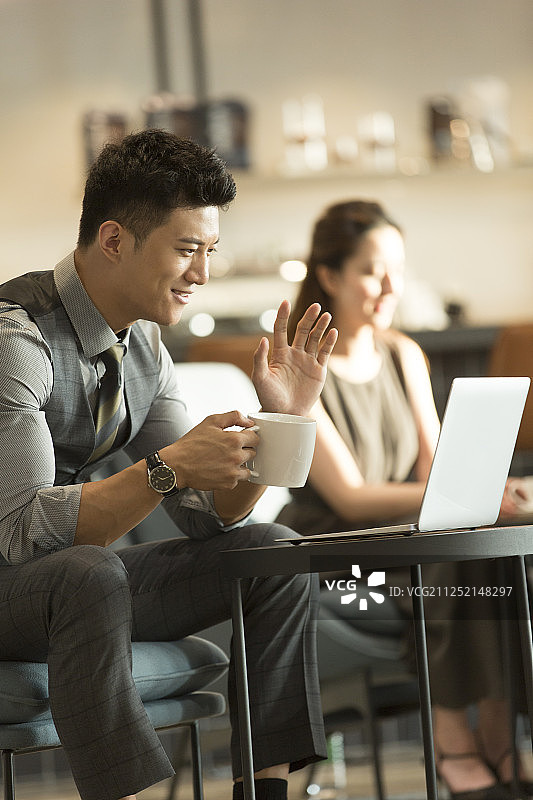 商务男子在咖啡馆喝咖啡使用笔记本电脑视频打招呼图片素材