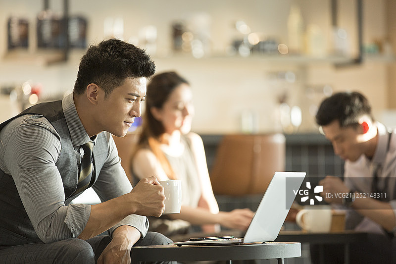 青年商务男子在咖啡厅喝咖啡使用笔记本电脑工作和两个青年商务男女喝咖啡吃饭聊天图片素材