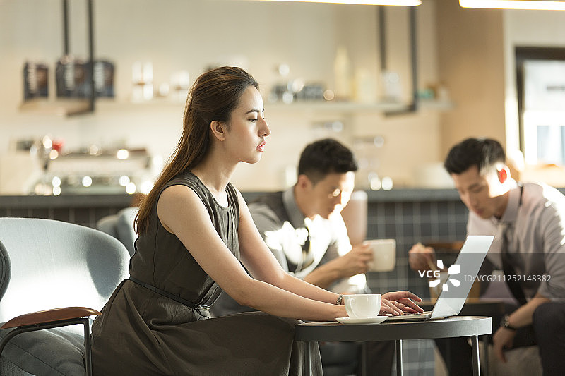 商务青年女子在咖啡厅使用笔记本电脑工作和两个青年商务男子喝咖啡吃下午茶聊天休闲图片素材