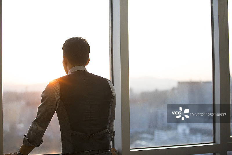 一个成功男商务人士站在办公大厦玻璃窗前思考看向窗外风景图片素材