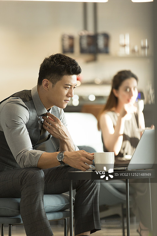 青年商务男子在咖啡厅喝咖啡整理领带使用笔记本电脑工作和青年商务女子喝咖啡休闲图片素材