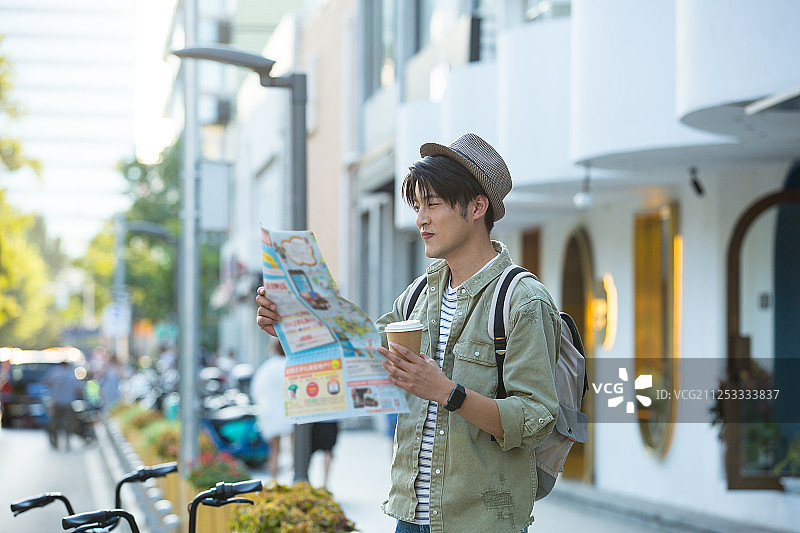 青年男子拿着咖啡看着旅游路线图在户外旅行度假图片素材