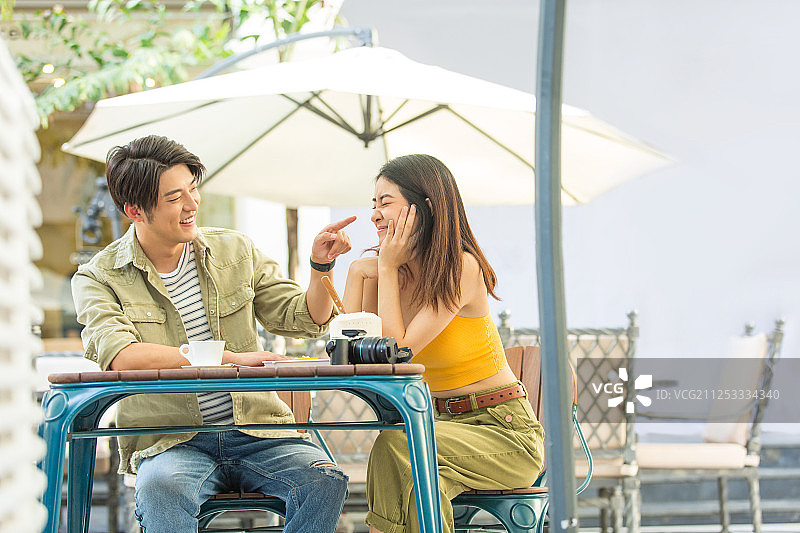 甜蜜情侣在户外咖啡店旅行休息喝咖啡吃甜品嬉戏打闹做鬼脸图片素材