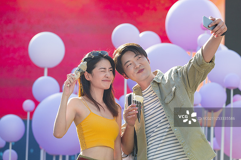 青年男女在户外步行商业街吃冰淇淋拿着手机自拍图片素材