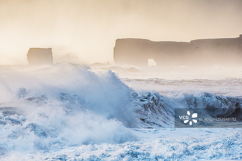 雾蒙蒙的日落下，海浪拍打海岸线图片素材