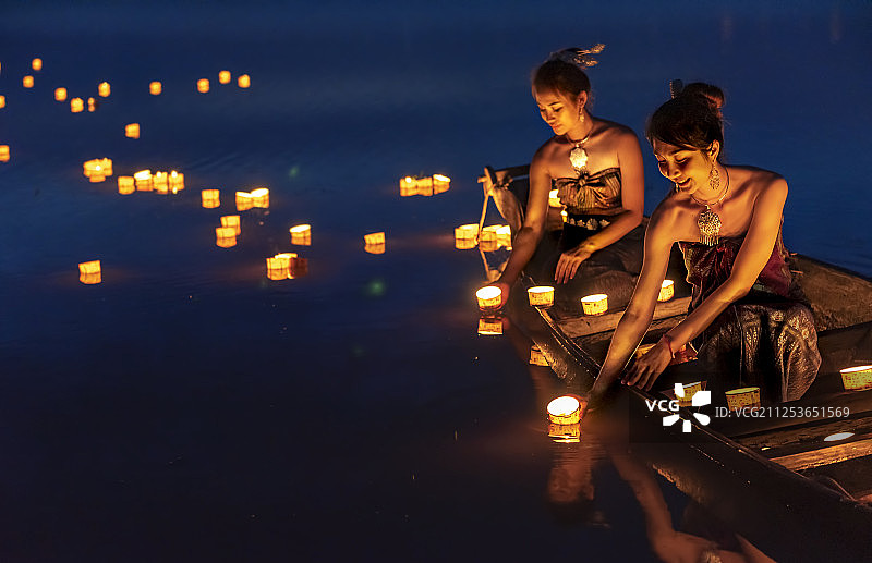 在水灯节期间，两个女人在夜晚将灯笼放在水上图片素材