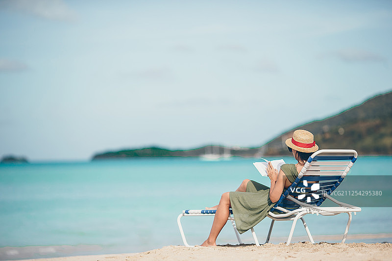 年轻女人在沙滩躺椅上看书图片素材