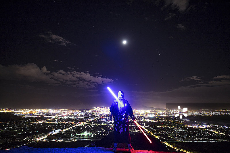 城市灯火前的一名背着发光剑的人图片素材