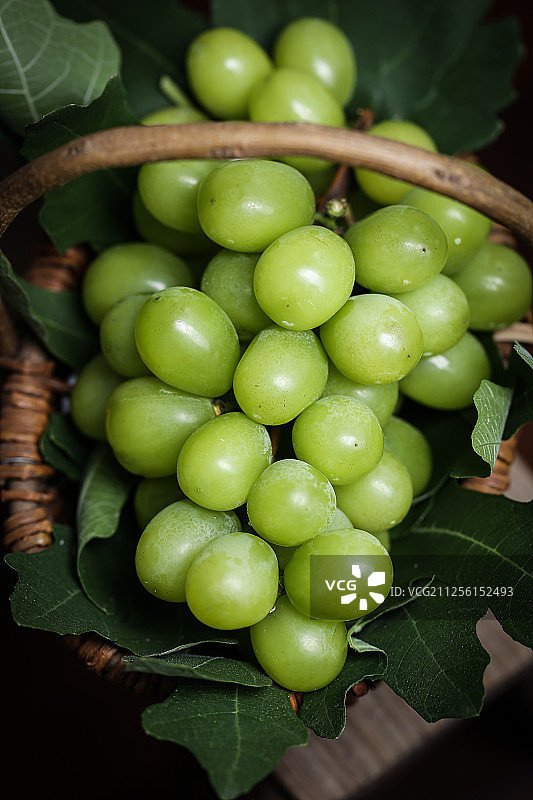 复古风格的放在竹篮里的新鲜阳光玫瑰青提葡萄图片素材