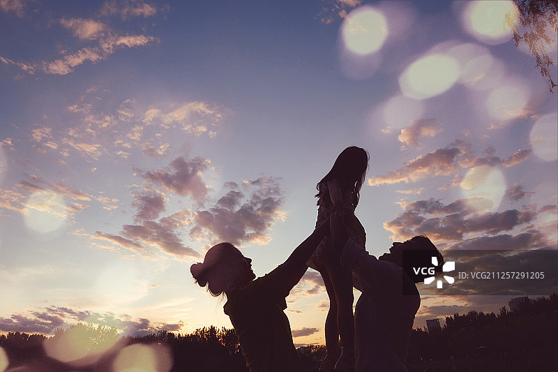 青年夫妇在夕阳下托起女儿图片素材