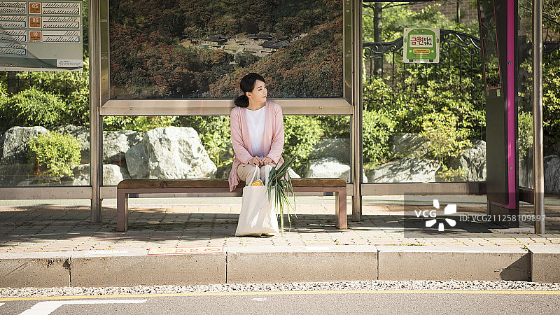 家庭主妇坐在长椅上，拿着购物袋等公交车摄影图片素材