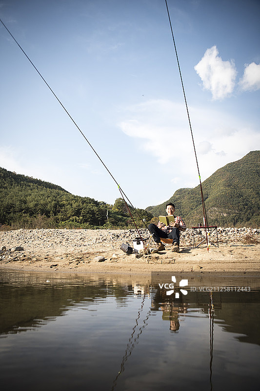 男人在河边读书和钓鱼的照片图片素材