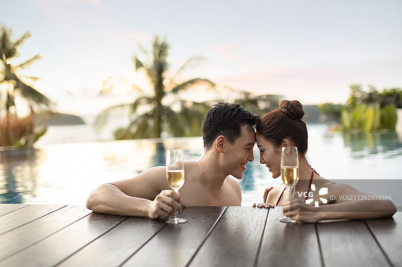 快乐的年轻情侣在泳池边喝香槟图片素材