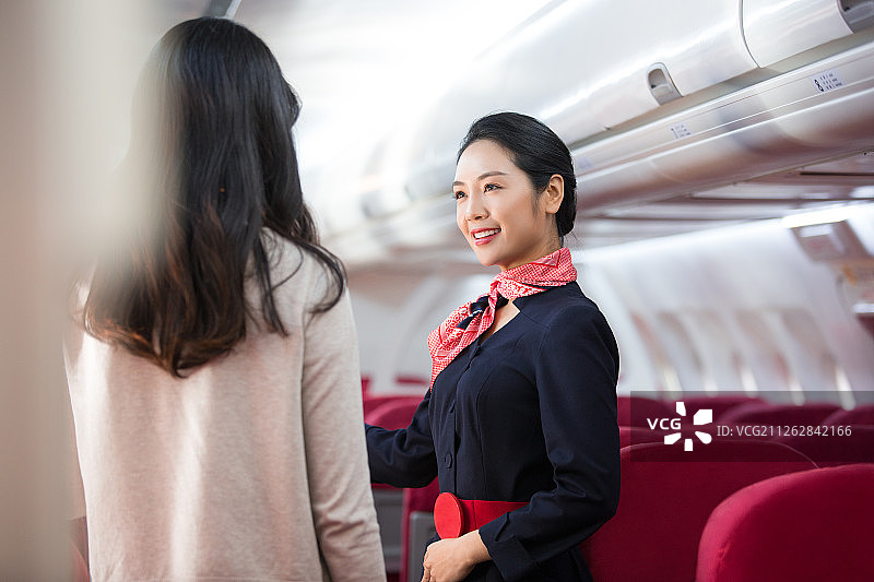 在飞机上年轻空姐帮助青年女乘客指引方向图片素材