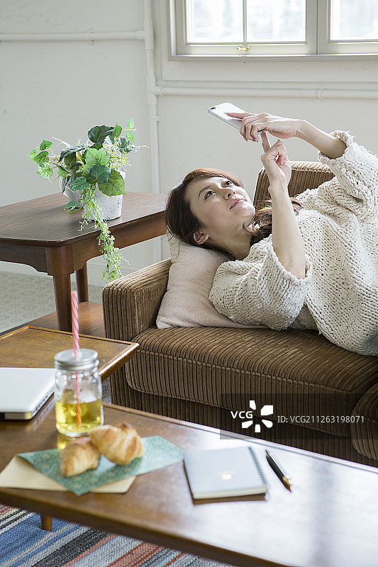中年女人躺在沙发上使用智能手机图片素材
