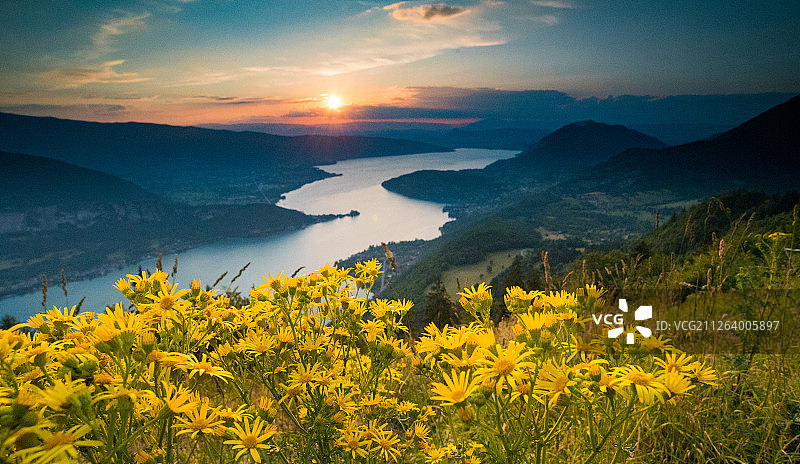 落日夕阳的湖光山色下，向前蜿蜒的河流和一簇野花图片素材