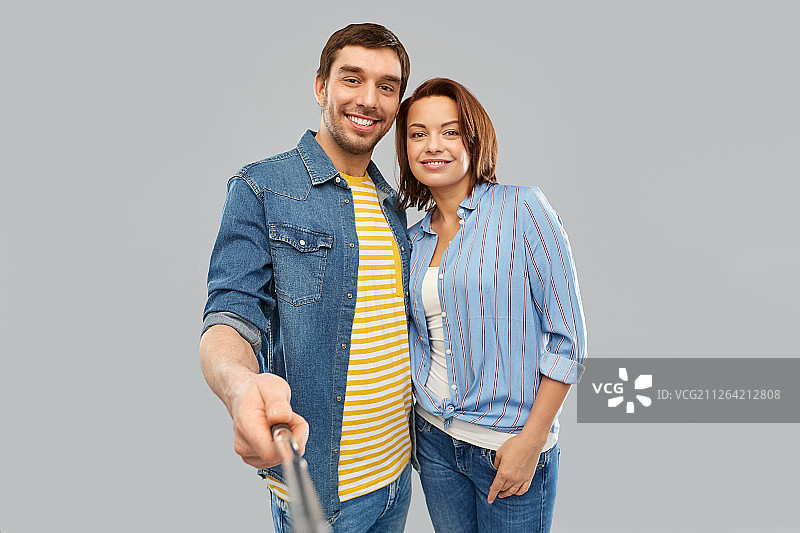 情侣使用自拍杆在灰色背景前拥抱拍照图片素材