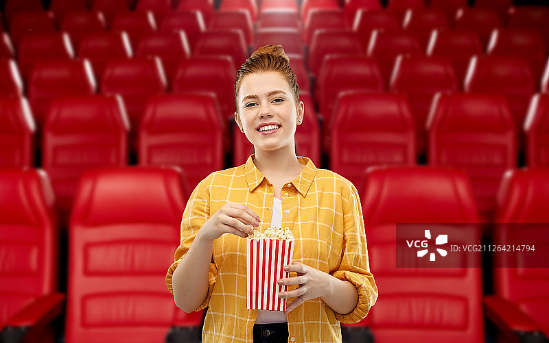电影院、快餐和娱乐概念——红发少女在电影院背景下吃爆米花图片素材