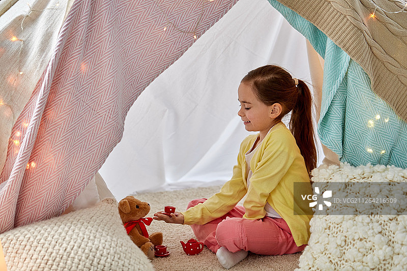 儿童与舒适概念：快乐的小女孩在家里的儿童帐篷里和泰迪熊玩茶话会图片素材