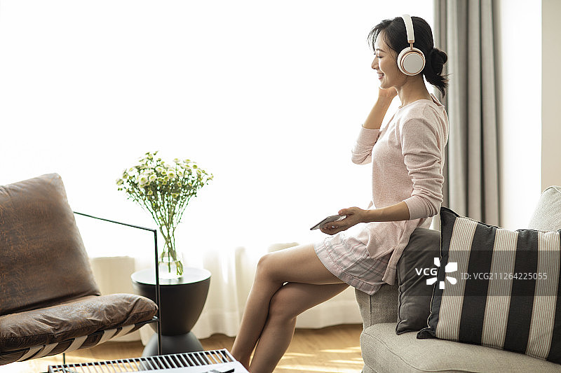 快乐年轻女士在家戴着耳机听音乐图片素材