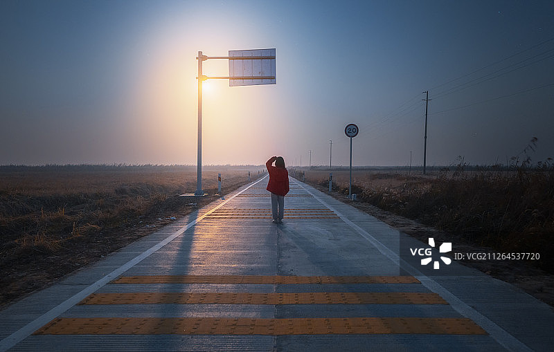满月升起时站在郊区乡村公路中间眺望远方天边的少女图片素材