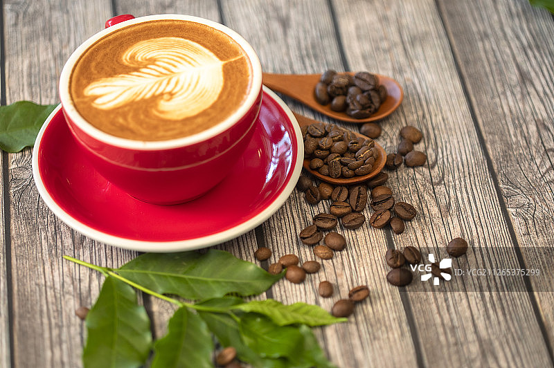 一杯含有叶子图案拉花的拿铁咖啡和咖啡豆图片素材